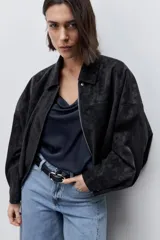 Campera marrón de poliuretano con acabado texturizado, silueta relajada, cuello camisero, cierre frontal, hombros caídos y mangas amplias con efecto abombado.