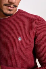 Sweater de punto grueso con cuello redondo y manga larga. Presenta un diseño de tejido acanalado y el logo de la marca bordado en el pecho.