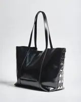 Cartera tote negra de símil cuero con acabado brillante, doble asa de hombro y detalles de tachas metálicas plateadas en los laterales.