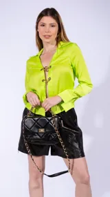 Blusa de satén color naranja, de manga larga con puños estructurados y cierre frontal mediante eslabones metálicos dorados.
