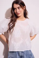 Blusa blanca traslúcida con estampado floral en relieve, cuello redondo y mangas globo cortas.