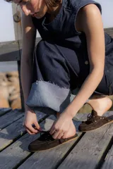 Zapatos tipo mocasín destalonados de gamuza marrón, estilo náutico con cordones frontales y ojales metálicos.