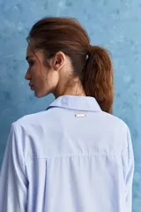 Camisa celeste de calce relajado, con cuello camisero, bolsillo aplicado en el pecho y mangas largas con puños abotonados. Cuenta con lazos ajustables en los laterales para fruncir y regular la silueta.
