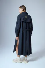 Trench midi negro confeccionado en algodón y nylon repelente al agua, con cuello clásico, cierre cruzado con botones, cinturón ajustable, mangas largas con puños abotonados, bolsillos internos altos y tajos laterales.