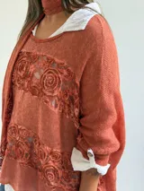 Sweater de punto color naranja con diseño holgado, que incorpora franjas horizontales de encaje con motivos florales. Presenta mangas tres cuartos con puños abotonados y se complementa con una bufanda del mismo tejido y color.