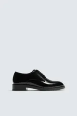 Zapato de vestir tipo derby de cuero negro brillante, con cordones y suela con ligero tacón.