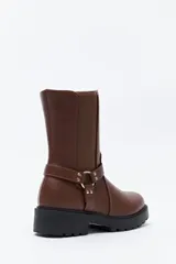 Bota tipo biker de caña media en cuero sintético negro, con panel elástico lateral, suela gruesa dentada y arnés decorativo con herraje metálico.