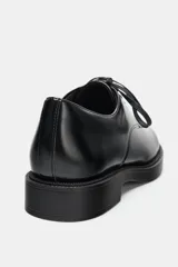Zapato tipo blucher de estilo clásico con cierre mediante cordones. Presenta un acabado en punta redonda y suela con plataforma.