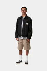 Campera Postal Jacket de Carhartt WIP en color negro, con cierre frontal de cremallera, cuello clásico, bolsillos laterales y un bolsillo con cierre en el pecho adornado con el parche del logo de la marca.