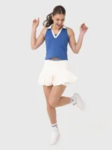 Conjunto deportivo compuesto por una musculosa azul con cuello polo y detalles en blanco, y una pollera short (skort) plisada de color blanco con cintura elástica.