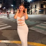 Vestido largo color beige con escote halter, corte ajustado y aberturas en la zona del abdomen.