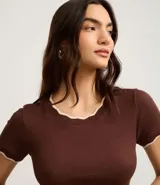 Top de manga corta ajustado al cuerpo, color marrón oscuro, con cuello redondo y bordes festoneados en color crema o beige claro.