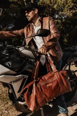 Bolso de cuero hecho a mano en color tostado, con diseño amplio y funcional. Presenta cierre superior, bolsillo frontal con cremallera, asas de mano reforzadas y una correa larga ajustable y desmontable.