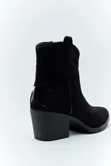 Bota corta de gamuza color negro, estilo texana, con taco cuadrado y puntera ligeramente perfilada. Presenta costuras decorativas en el empeine y tiradores laterales.