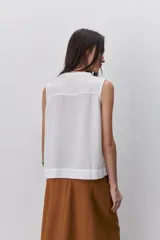 Blusa sin mangas color negro, de silueta fluida, con cuello redondo, detalle de alforzas en el frente y abotonadura parcial con botones visibles.