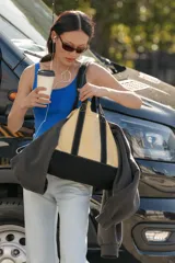 Bolso shopper de lona color beige con base, asas y tiras frontales en color negro. Cuenta con un bolsillo frontal con botón a presión y costuras visibles en contraste.