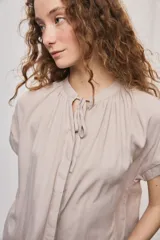 Camisa de manga corta color celeste, confeccionada en viscosa fluida, con silueta amplia y escote redondo con frunces y lazo para anudar.