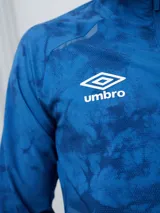 Campera deportiva Umbro del Club Nacional de Football, modelo Grok, en color bordó con diseño estampado sutil. Cuenta con cierre frontal completo, cuello alto y bolsillos laterales.