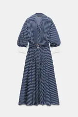Vestido midi azul marino con rayas blancas, cuello solapa, escote en V y cierre frontal con botones. Cuenta con mangas abullonadas por debajo del codo con puños anchos a contraste, cinturón ajustable del mismo tejido con hebilla metálica y falda evasé.