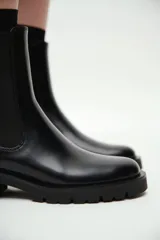 Botas Chelsea negras de cuero sintético con elásticos laterales y suela track gruesa. Tienen un tacón bajo y ancho, y una trabilla en la parte trasera del caño.