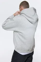 Canguro gris con capucha forrada con cordón ajustable, hombros caídos, bolsillo tipo canguro y corte holgado.