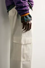 Pantalón cargo relaxed fit de color blanco, confeccionado en tejido de algodón. Presenta bolsillos de plastrón con solapa en las perneras y cierre frontal con cremallera y botón.