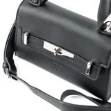 Cartera pequeña de mano tipo bandolera, confeccionada en símil cuero negro con textura saffiano. Presenta una solapa frontal con cierre de broche metálico plateado y el logo de la marca grabado en la parte inferior. Incluye asa superior fija y correa larga regulable y extraíble.