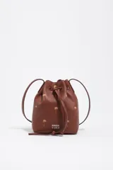 Bolso tipo bucket Bimba y Lola modelo Carlino, confeccionado en cuero marrón con estampado de pequeñas palmeras doradas y logo impreso en la parte frontal. Cuenta con cierre de cordón ajustable y asas largas para llevar al hombro.