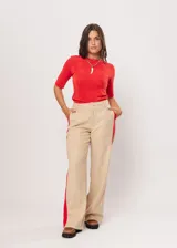 Pantalón beige de tiro alto con bolsillos delanteros y traseros, cierre frontal con cremallera y botón, y detalle de pespuntes rojos en los laterales.