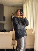 Sweater de punto con silueta holgada y cuello a la base, confeccionado en una mezcla de algodón y lurex que le otorga un acabado brillante. Presenta un diseño con aberturas laterales en el ruedo y puños acanalados.