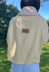 Campera de gamuza color beige con interior y detalles de corderito sintético en cuello y puños. Presenta cierre frontal con botones tipo toggle de madera y cuero, y bolsillos frontales.