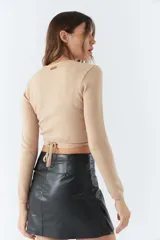 Top tejido de punto con diseño cruzado, escote en V y mangas largas. Cuenta con tiras para anudar en la cintura y detalle de grifa de cuero.