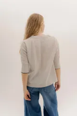 Buzo básico de lambswool color gris oscuro, con escote en V y mangas 3/4. Presenta un fit amplio y tajos laterales. Los puños tienen un detalle de ribete en color celeste y amarillo.