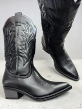 Bota estilo texano de caña alta, color negro, con costuras decorativas en el empeine y en la caña. Presenta un taco cuadrado de altura media y punta ligeramente afinada.