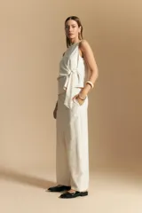 Pantalón ancho de tiro alto, color blanco roto con finas rayas verticales en color beige/marrón. Presenta un detalle de nudo o lazo en la cintura.