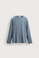 Camiseta relaxed fit de manga larga confeccionada en tejido waffle con mezcla de algodón y cáñamo. Presenta cuello redondo con cierre frontal parcial de botones.