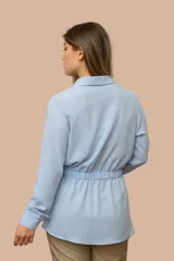 Camisa de seda color celeste, con cuello camisero, mangas largas y lazo ajustable en la cintura que genera un efecto fruncido.