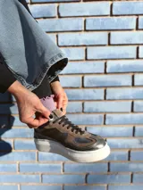 Zapatillas deportivas de cuero color peltre, con cordones negros y suela de goma blanca.