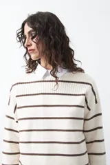 Sweater de tejido de punto con diseño de rayas horizontales en color marrón sobre fondo crudo. Presenta cuello redondo, puños y ruedo acanalados, con hombros caídos y silueta relajada.