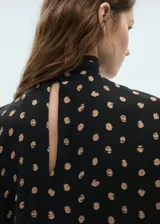 Blusa de viscosa con cuello alto drapeado y mangas cortas. Presenta un diseño recto con estampado de topos en tonos contrastantes sobre fondo negro.