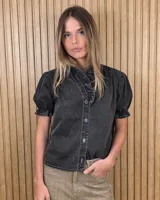 Camisa de denim de algodón celeste, con cierre frontal de botones, cuello alto con volados y mangas cortas abullonadas con puños elastizados fruncidos.