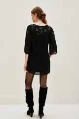 Vestido corto negro con bordados y aplicaciones de lentejuelas en el pecho y mangas, de corte holgado y mangas tres cuartos.