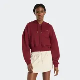 Campera con capucha y cierre frontal, color rojo oscuro (bordó), de corte cropped y calce holgado. Presenta un pequeño logo de New Balance bordado en el pecho izquierdo.