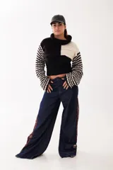 Polera corta de tejido artesanal con diseño bicolor en blanco y negro. Presenta cuello alto, mangas largas con trama a rayas y etiqueta de marca en la parte posterior.