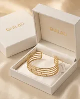 Set de cuatro brazaletes tipo esclava de acero con baño de oro, con textura martillada y detalle de circonias incrustadas.