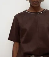 Remera de corte regular confeccionada en gamuza sintética color negro, con mangas cortas y cuello redondo decorado con una aplicación de pedrería brillante.