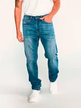 Jeans de mezclilla azul con calce slim, diseño clásico de cinco bolsillos, cierre de cremallera y botón metálico. Presenta efecto desgastado en los muslos y costuras en tono contrastante.