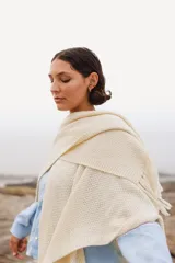 Ruana de lana merino color crudo, con textura tejida y terminación de flecos en los extremos.