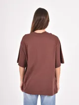 Remera de corte oversize color beige, con cuello redondo y mangas cortas. Presenta un estampado frontal con la frase 'Amore Mio', un dibujo de dos cerezas y la leyenda 'South Tuscany Italy'.