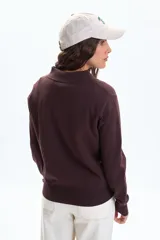 Buzo de punto color marrón, con cuello polo y cierre frontal de tres botones, de manga larga y puños ajustados.